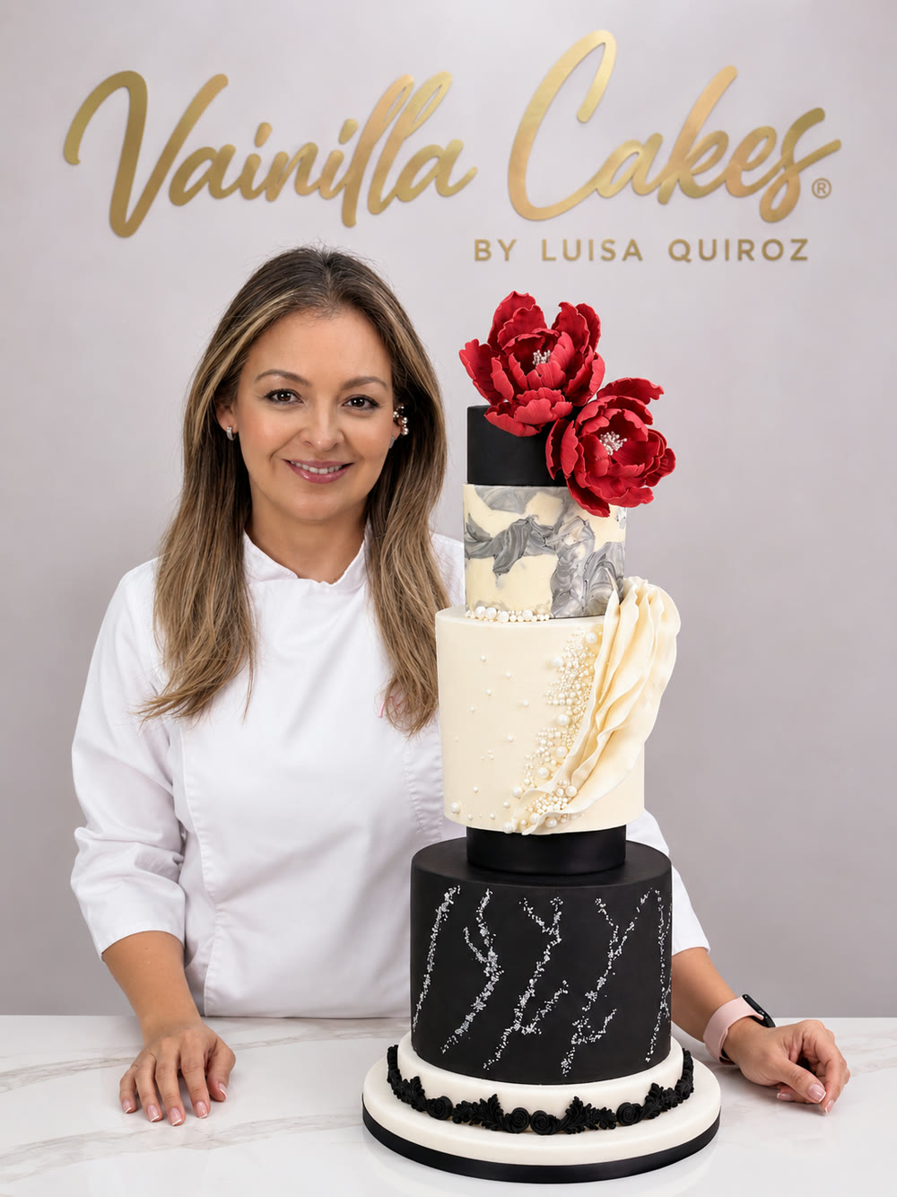 Luisa Quiroz junto a la torta del proyecto: tres pisos en buttercream con ruffles marfil, perlas, escamas plateadas y peonías rojas